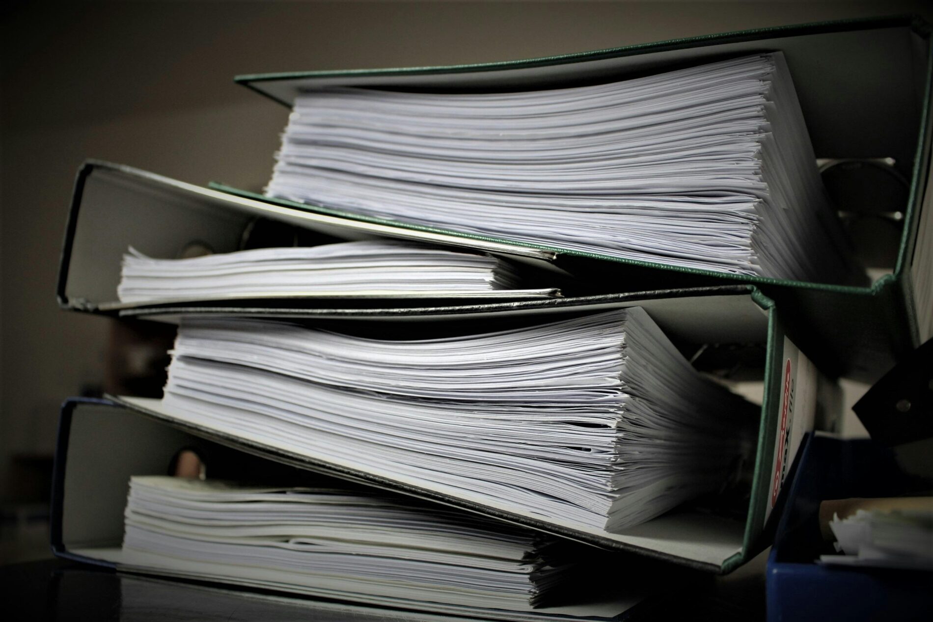 HEALTHCARE RECORDS Three thick binders filled with stacks of paper are stacked on top of each other on a table.