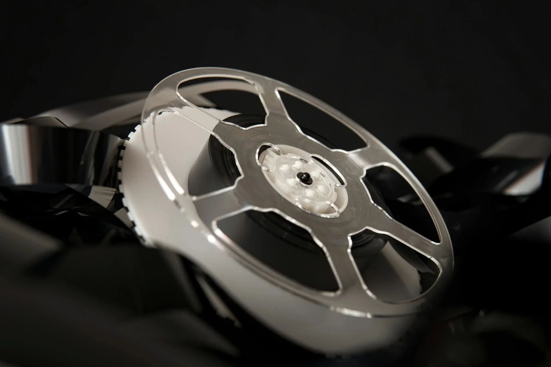 films are properly prepared Close-up of a metallic film reel with black filmstrip against a dark background.
