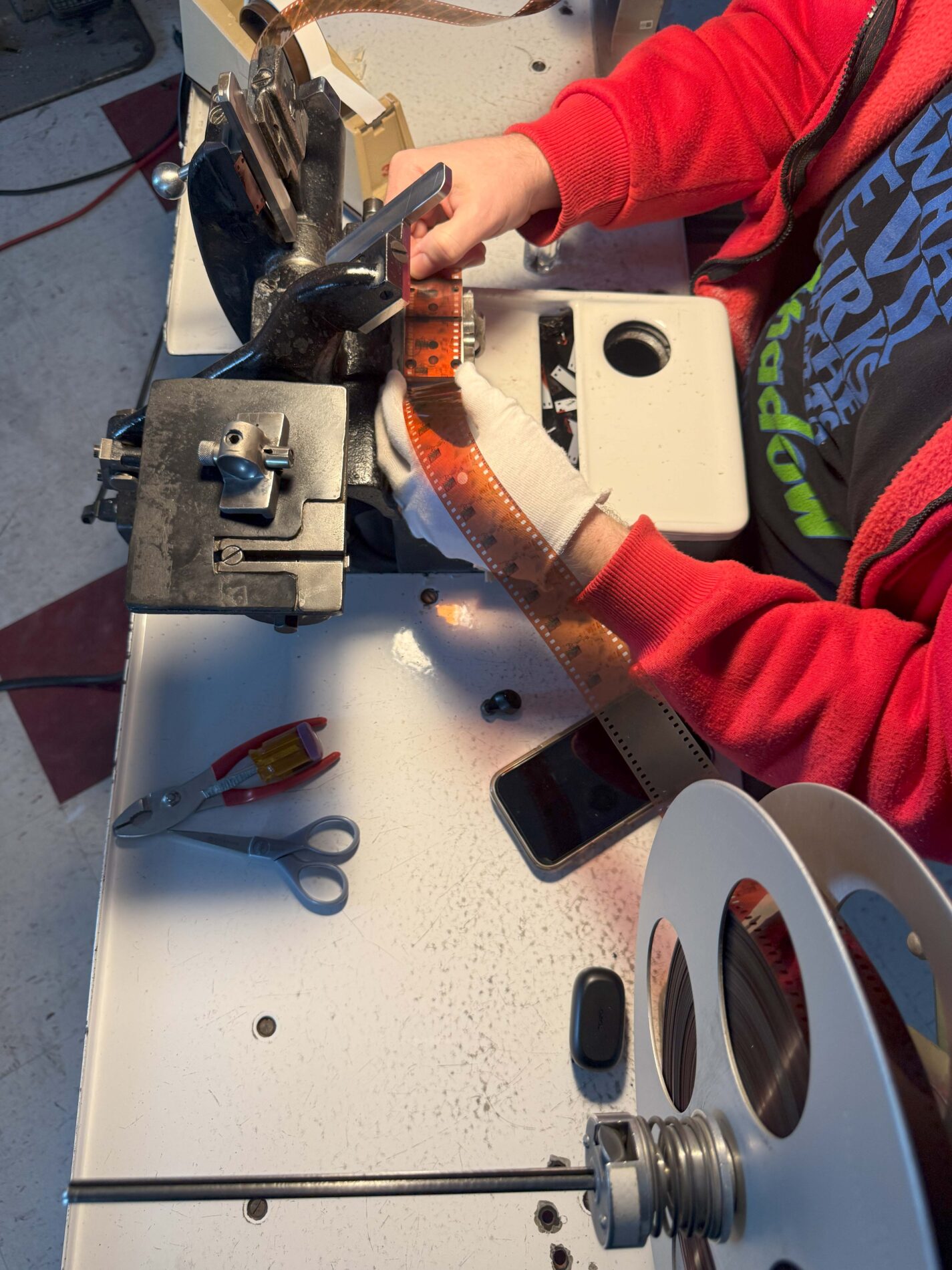 FILM INSPECTION Person wearing gloves splices a strip of film on a splicing machine, with scissors and a phone on the table.