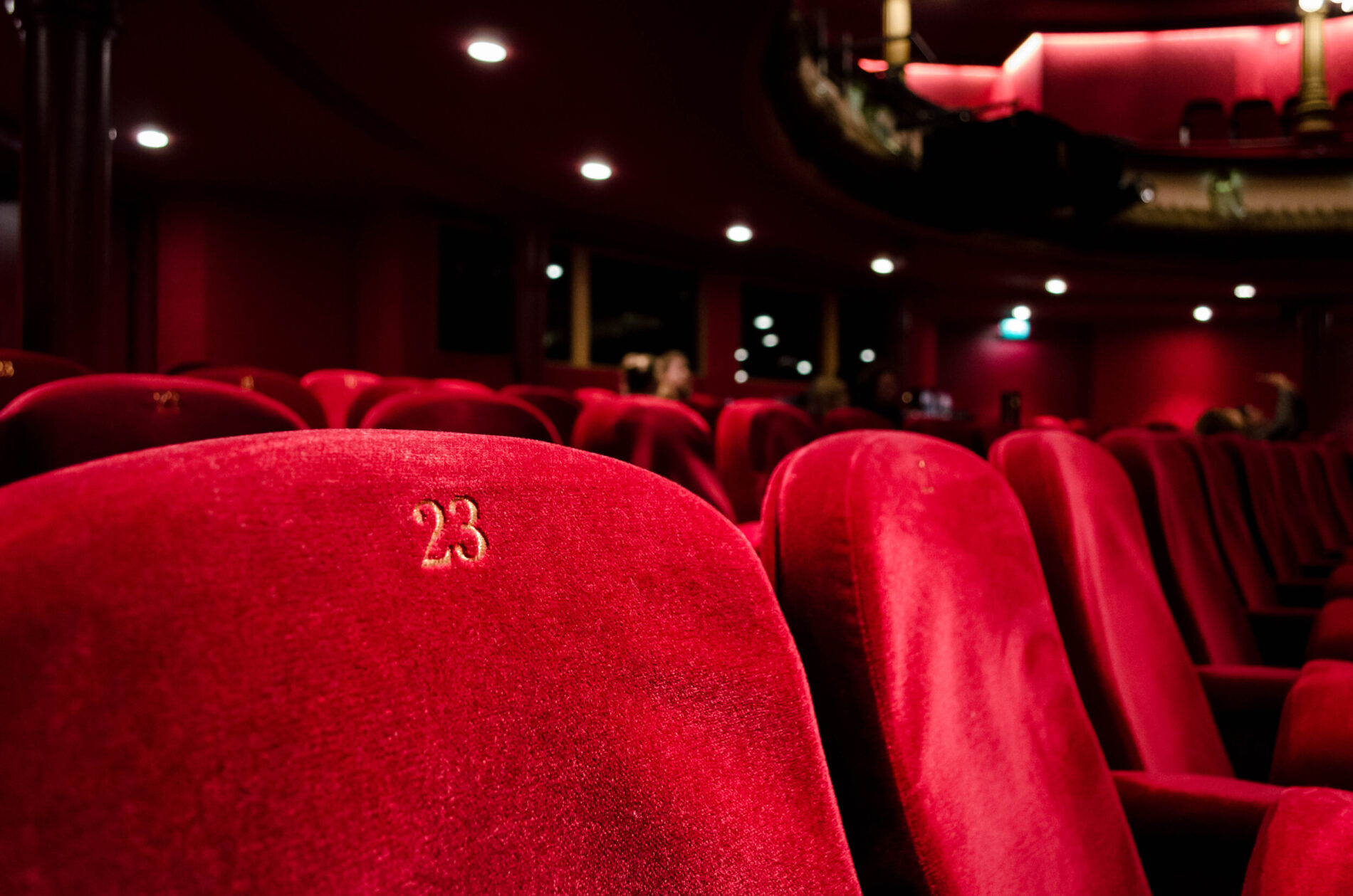 Marketing Red velvet theater seats with the number 23 embroidered, in an empty or sparsely occupied auditorium.