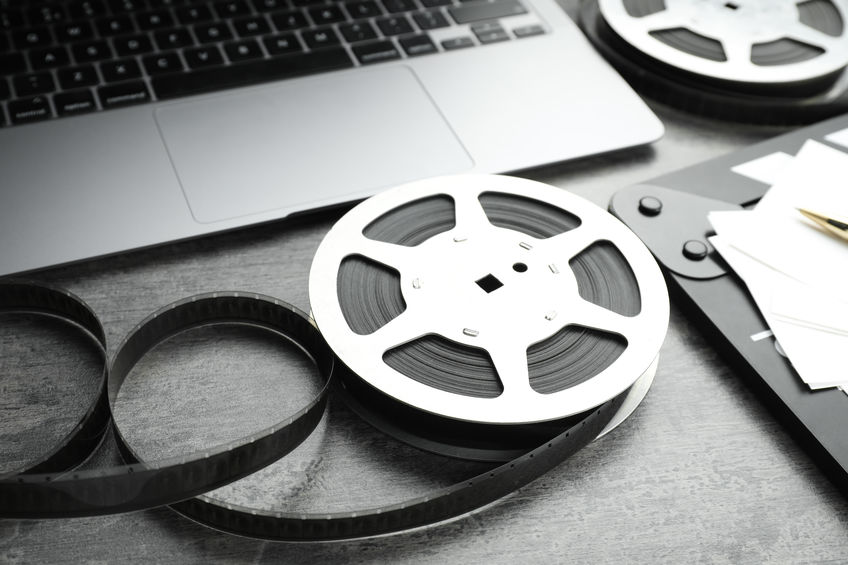 Film reels and laptop on grey textured table, closeup A film reel sits partially unwound next to a laptop and papers on a gray table.