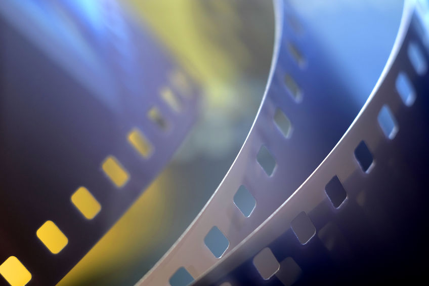 Asset Migration Close-up view of two strips of photographic film with sprocket holes, shown in soft focus and blue-yellow lighting.