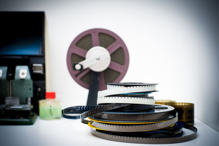 A vintage 8mm movie editing desktop with reels and elements in o A stack of film reels sits on a table with editing equipment and a larger reel in the background.
