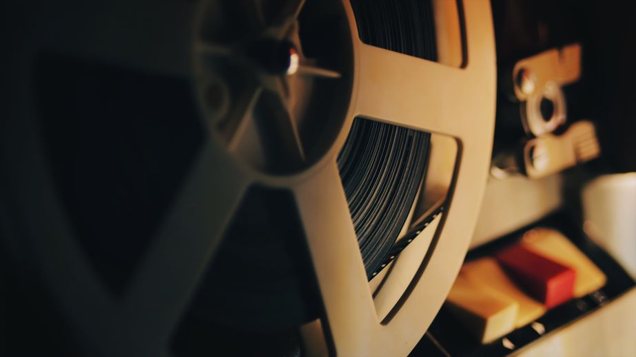 Old 8mm film projector playing in the night. Close-up of a reel with a film. Close-up of a reel-to-reel tape recorder showing a tape reel and control buttons.