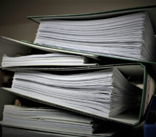 Three thick binders filled with stacks of paper are stacked on top of each other on a table.